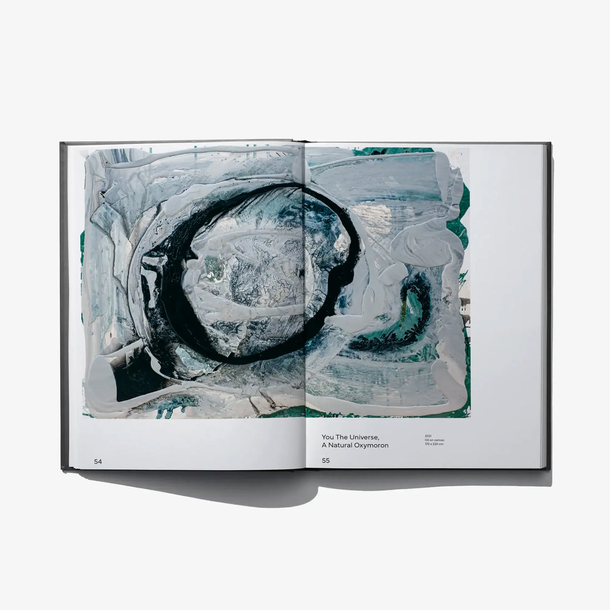 Open art book spread with large black circle artwork over blue-gray painted pages