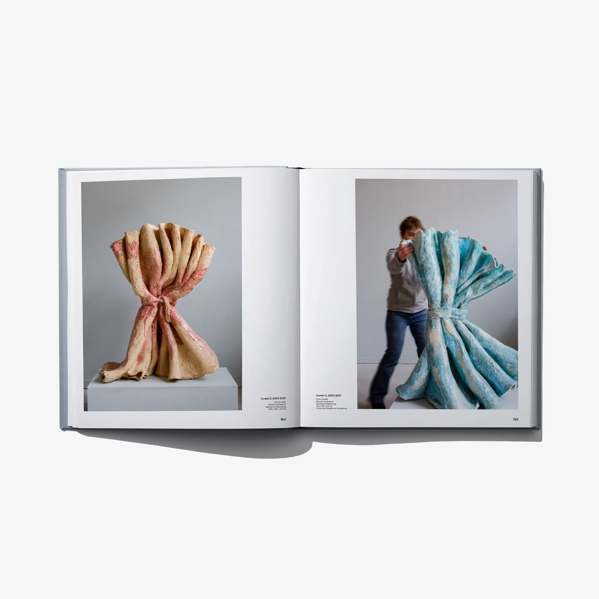 Open hardcover art book with nude-toned sculpture photo and a person draped in fabric