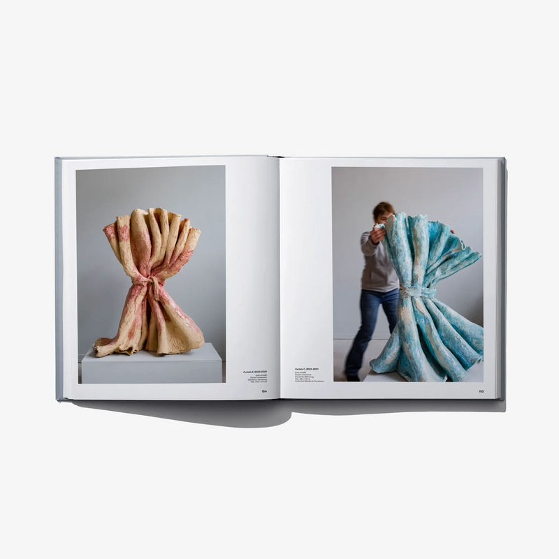 Open hardcover art book with nude-toned sculpture photo and a person draped in fabric
