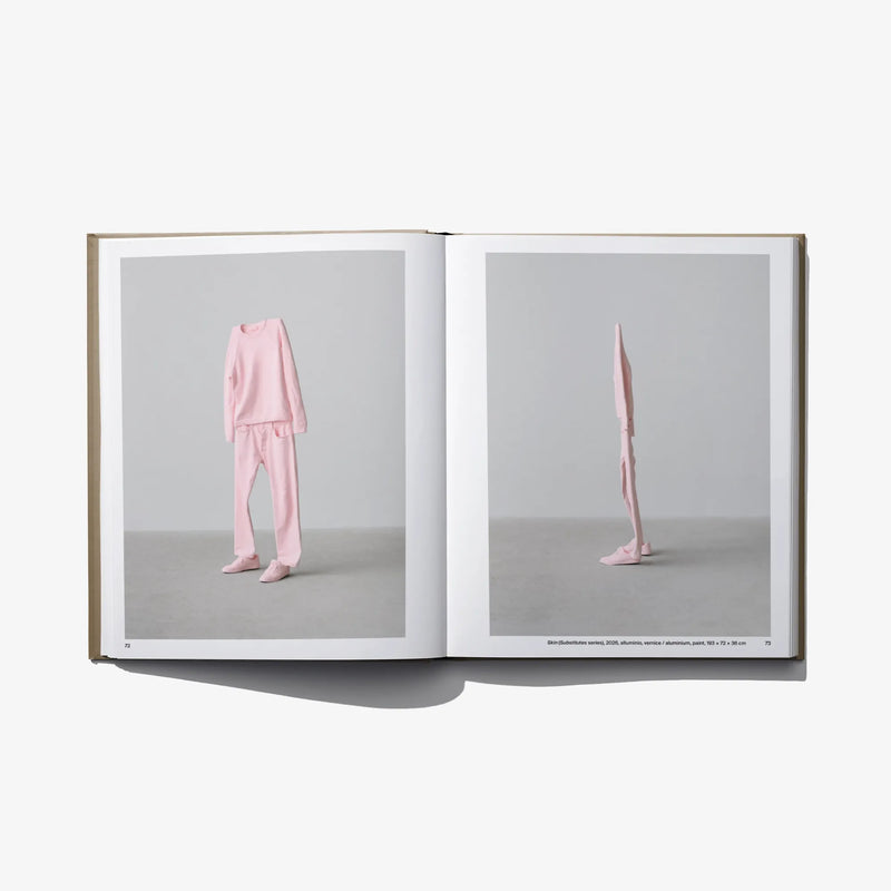 Open art book with a pink-clad figure standing on right page.