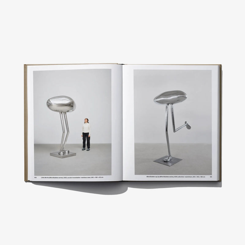 Open art book with chrome stool sculptures and a standing person on pages.