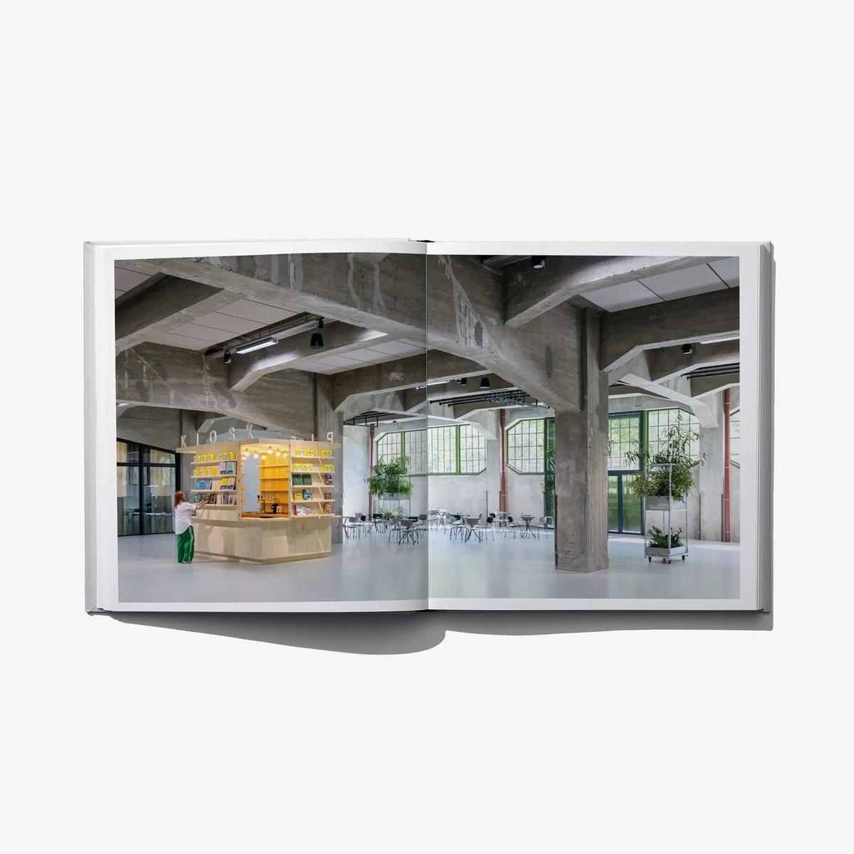 Open architecture book showing an indoor museum hall with concrete columns and seating.