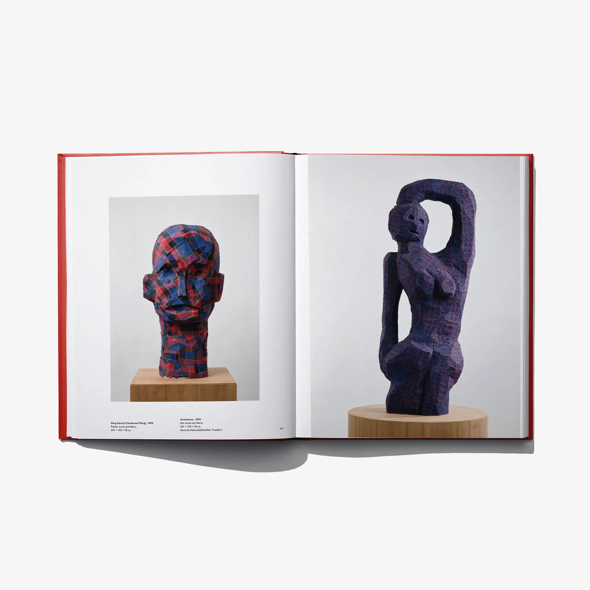Open art book with two dark blue figurative sculptures on display stands