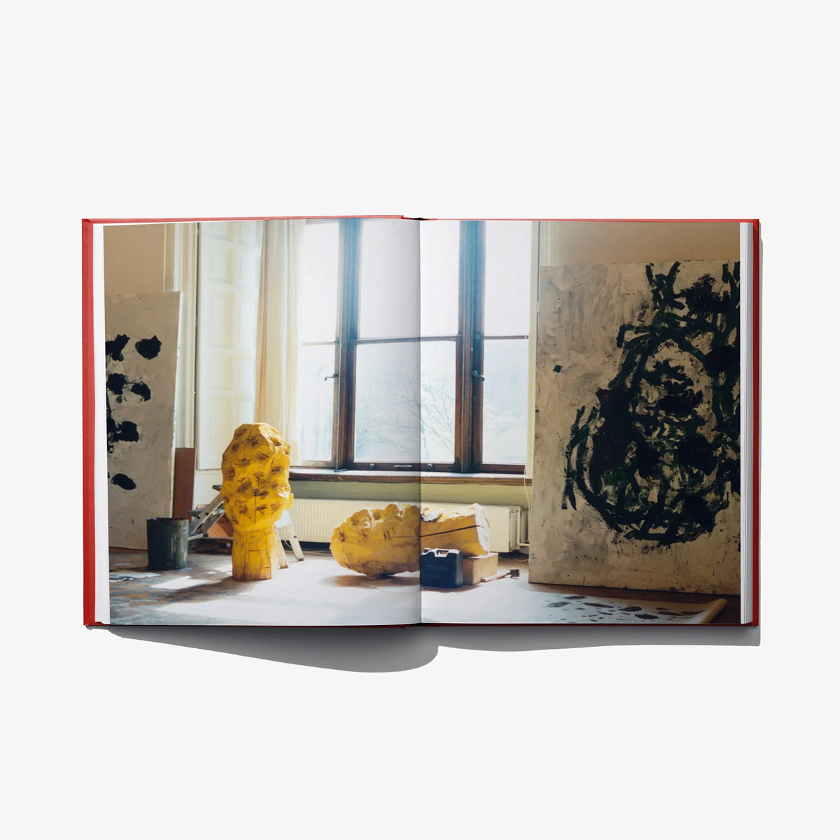 Open art book with yellow sculptural figures in an exhibition photo