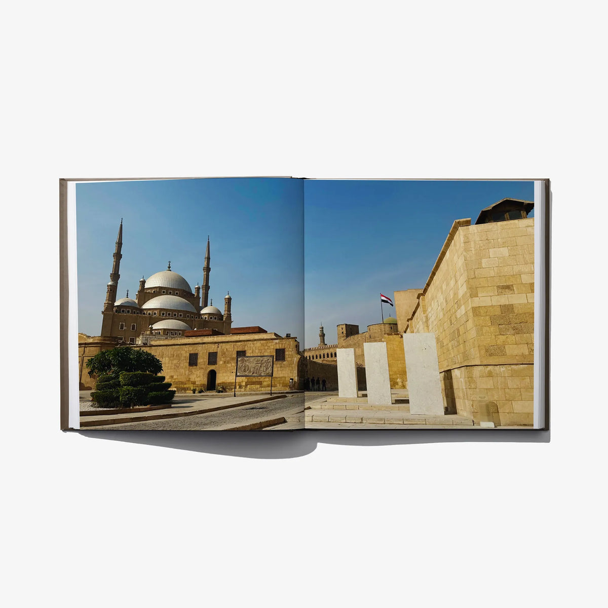 Open hardcover art book featuring mosque imagery on left and stone building on right