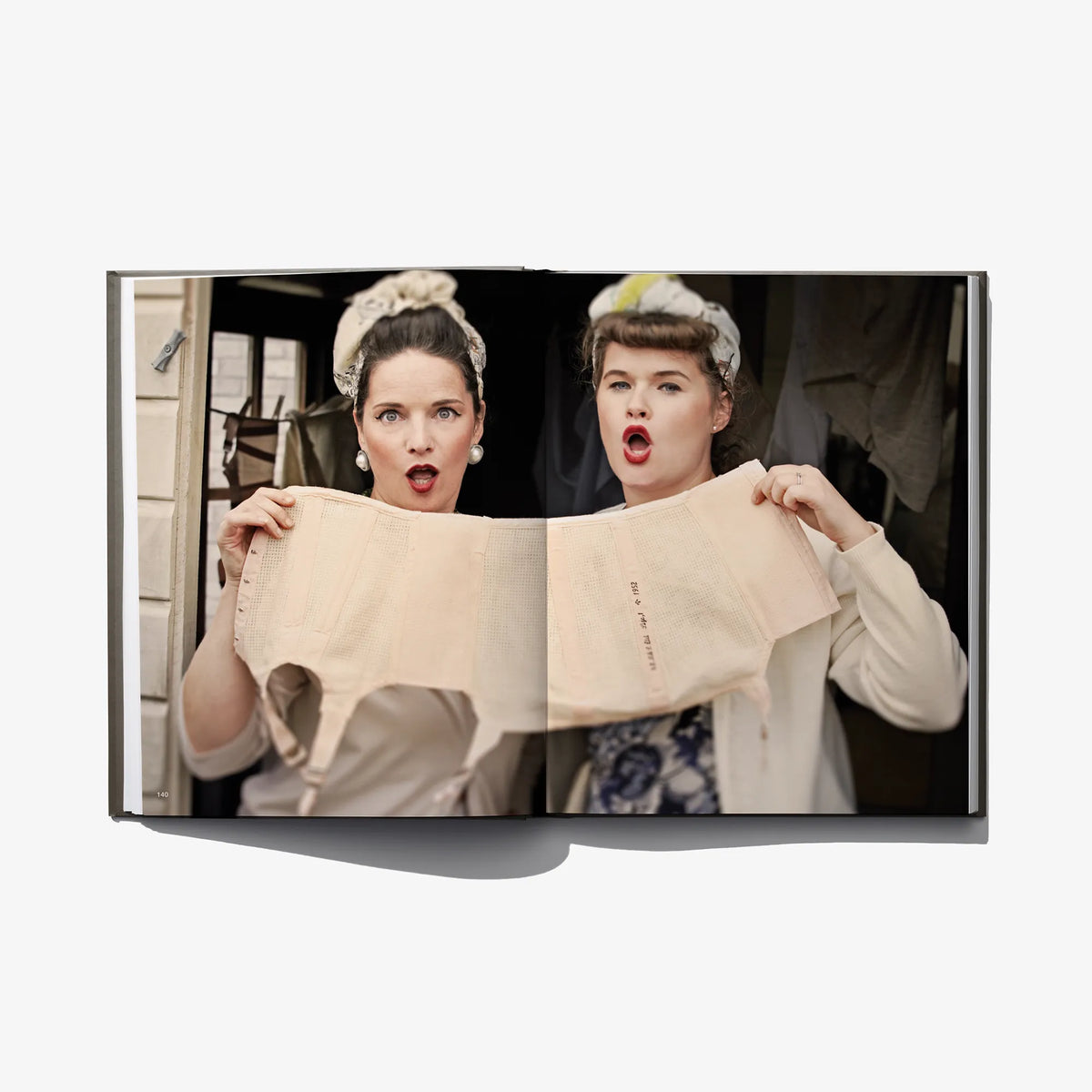 Photo book spread with two women holding a light beige fabric garment