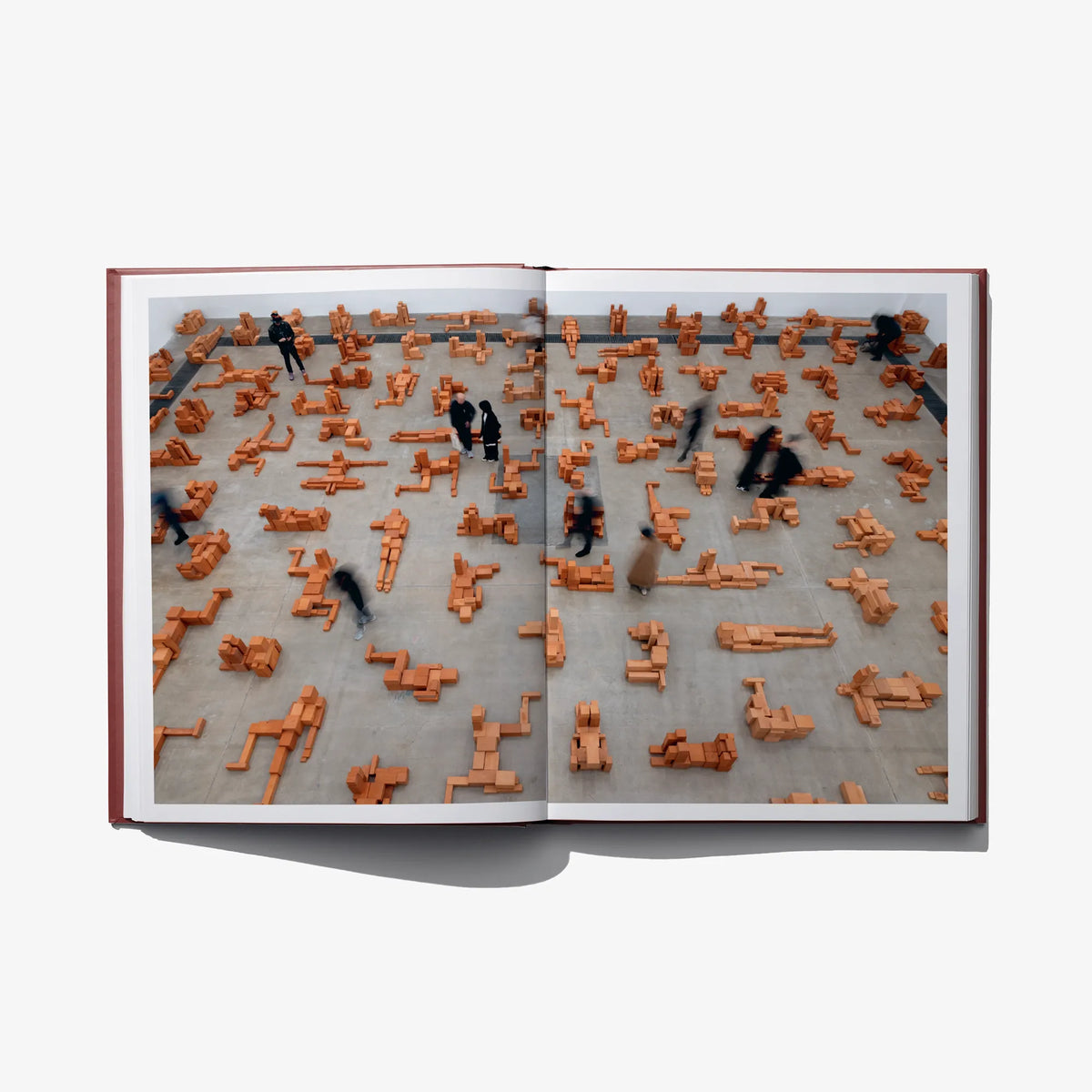 Open book spread showing a large arrangement of small orange figure-like sculptures.