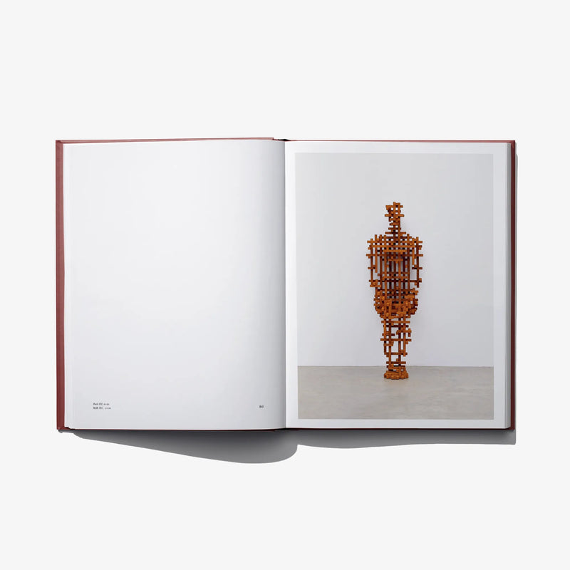 Open book spread with a single tall standing orange figure sculpture on the right page.