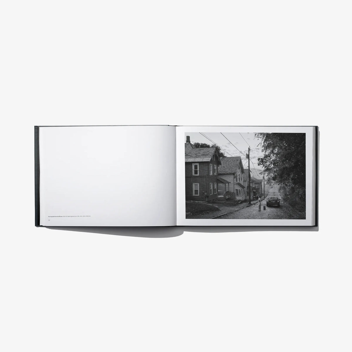 Open photo book spread with blank left page and black-and-white neighborhood street photo