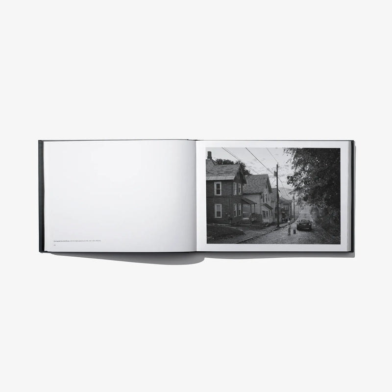 Open photo book spread with blank left page and black-and-white neighborhood street photo
