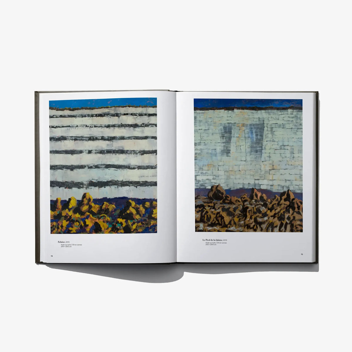 Open art book with two painted scenes: striped buildings on the left, crowd near a wall on the right.