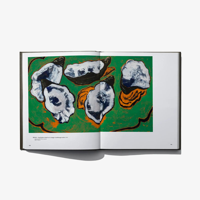Open art book with an illustration of abstract face-like shapes on a green background.