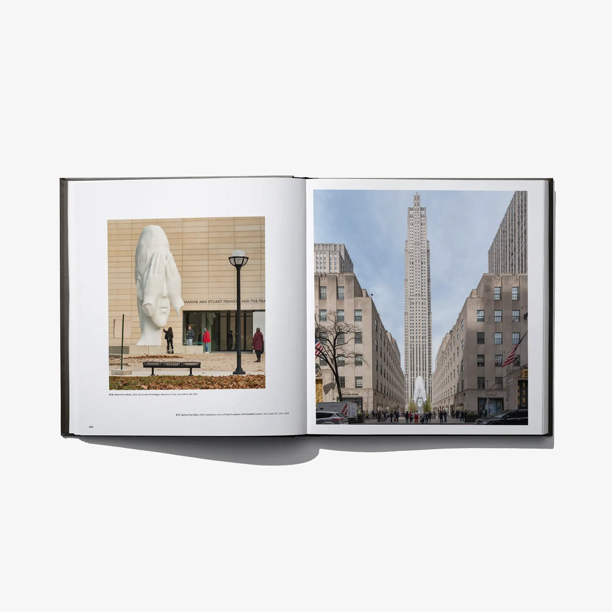 Open art book with a white sculpture in a plaza and a tall city skyscraper view.