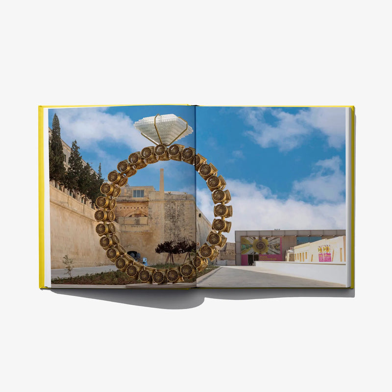 Open art book spread featuring a large gold circular sculpture outdoors against sky.