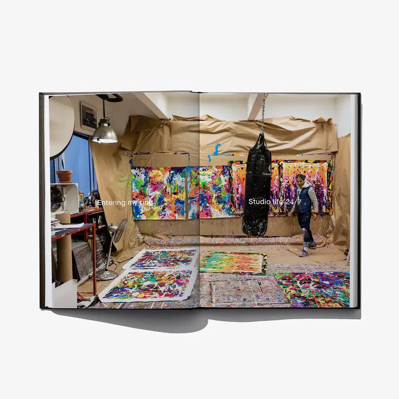 Open art book spread showing a studio scene with multiple colorful paintings
