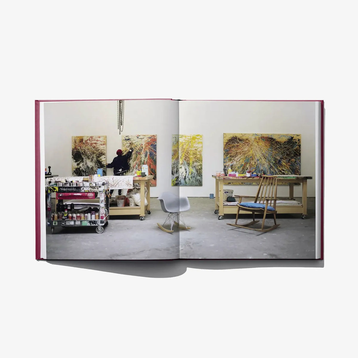 Open hardcover art book with studio photos of paintings, tables, and easels