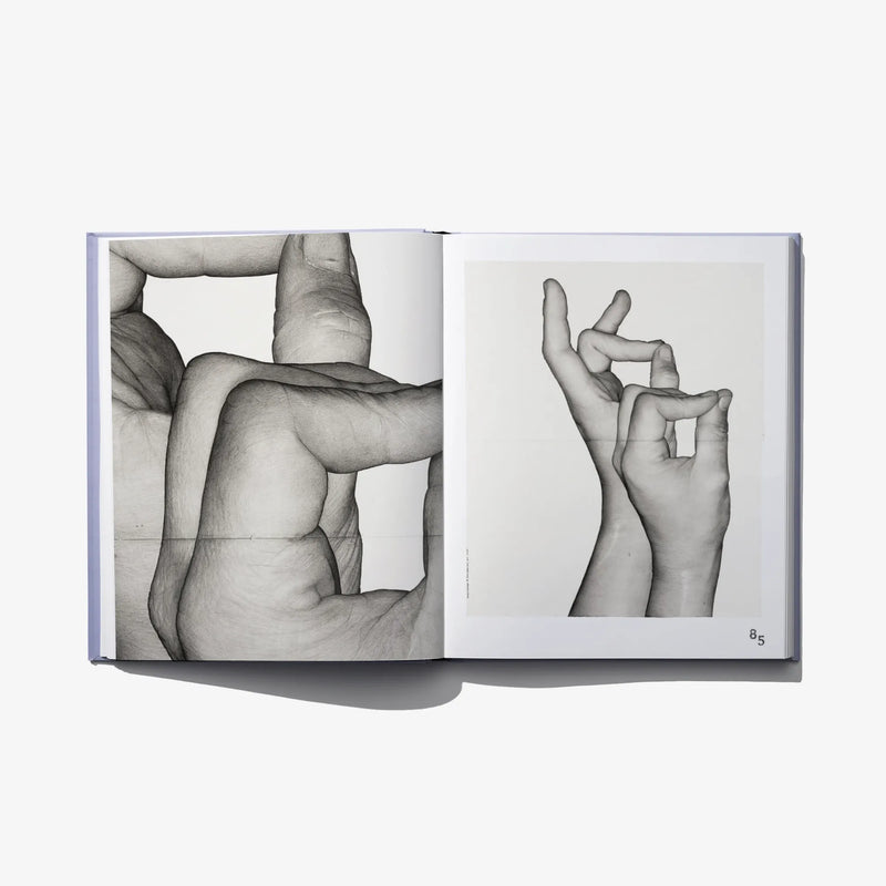 Open art book spread showing black-and-white hands and legs figure study