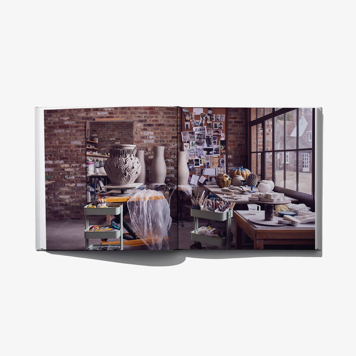 Open art book spread with studio room photo, shelves, and framed objects