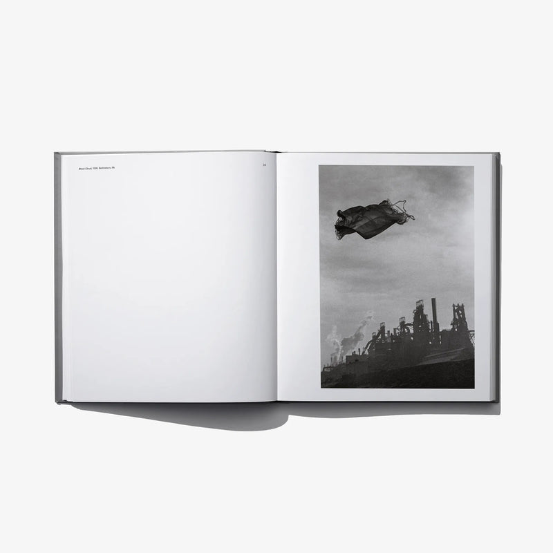 Open photo book spread with blank left page and grayscale photo of cloth above smokestacks