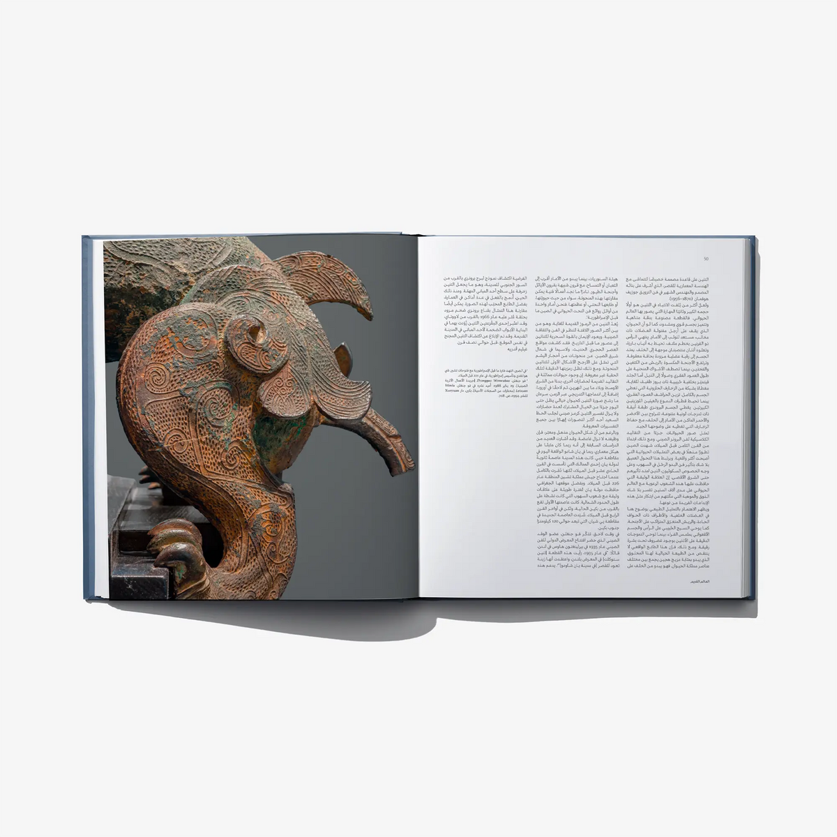 Open art book spread featuring a detailed bronze animal sculpture and Arabic text