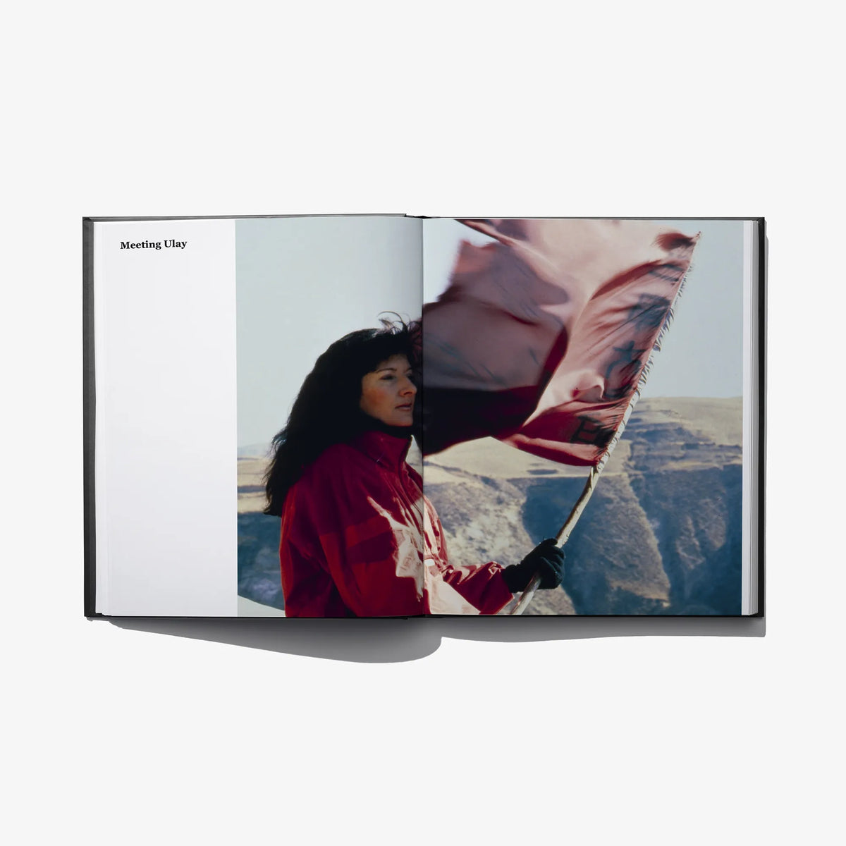 Open art book spread showing person holding a large fabric flag