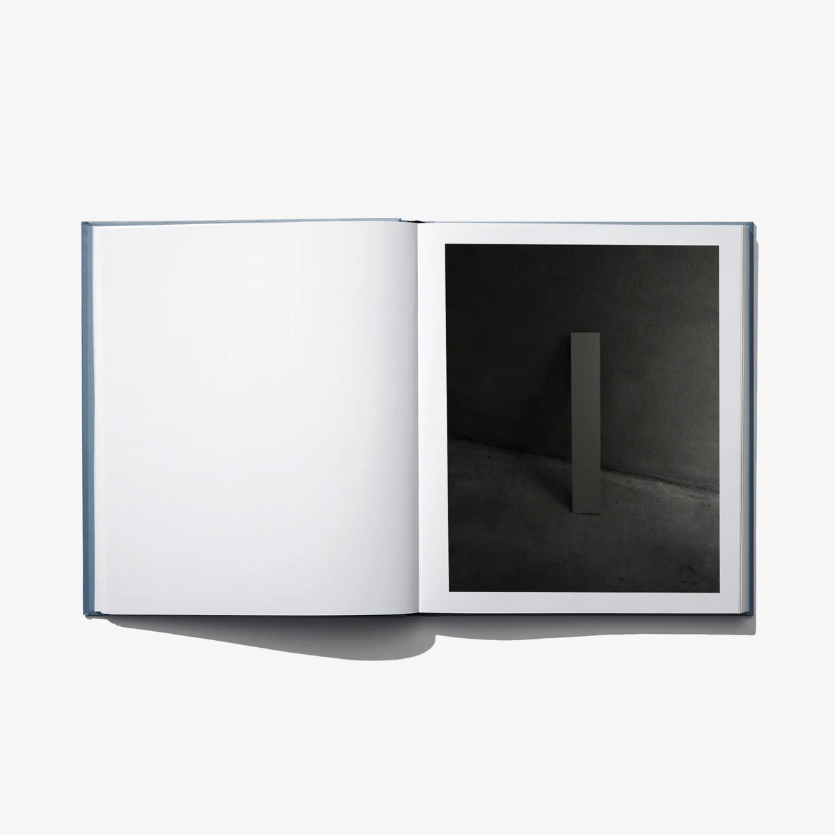 Open art book with blank white left page and a dark room photograph on right page.