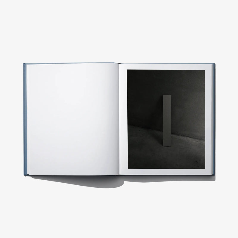 Open art book with blank white left page and a dark room photograph on right page.