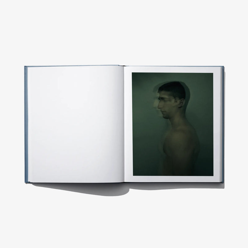 Open art book with blank white left page and a green portrait photograph on right page.