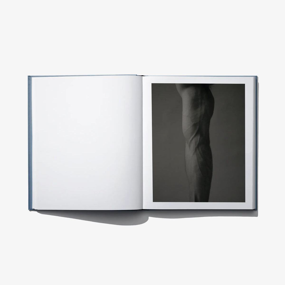 Open art book with blank white left page and a black-and-white figure photograph on right.