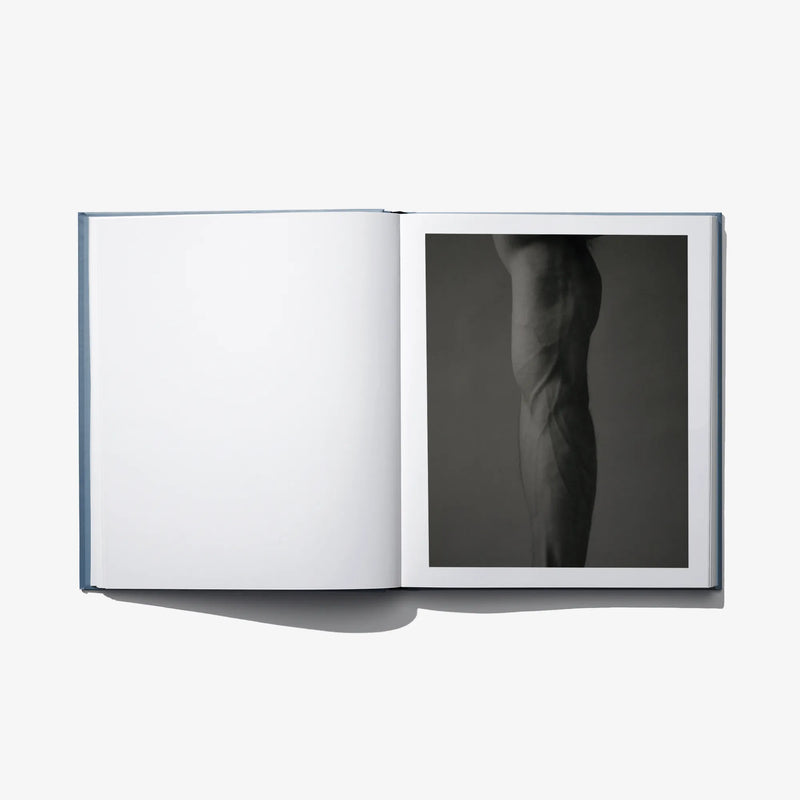 Open art book with blank white left page and a black-and-white figure photograph on right.