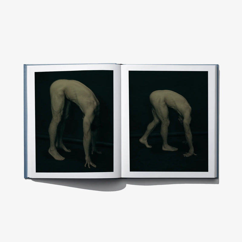 Open art book showing two black photo panels with posed nude figures on the right pages.