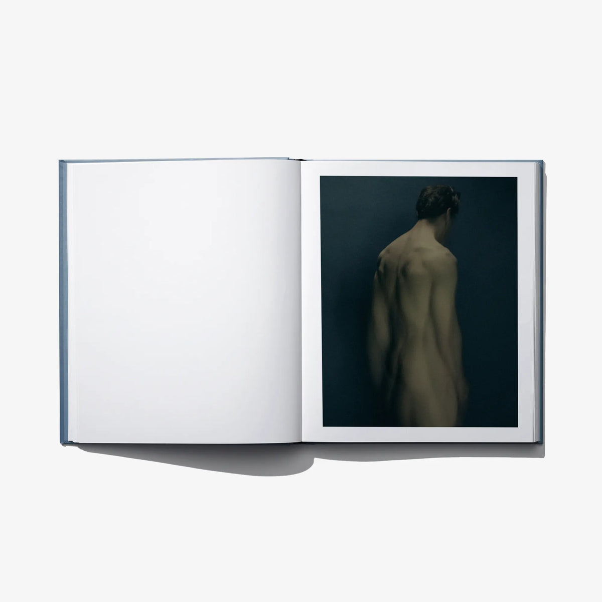 Open art book with blank white left page and a back-view figure photograph on right.