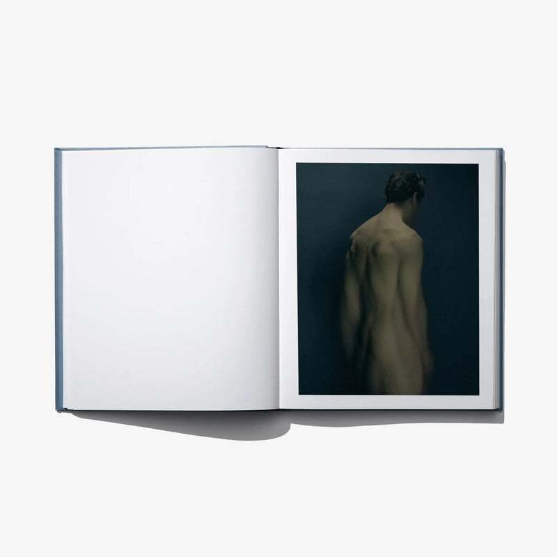 Open art book with blank white left page and a back-view figure photograph on right.