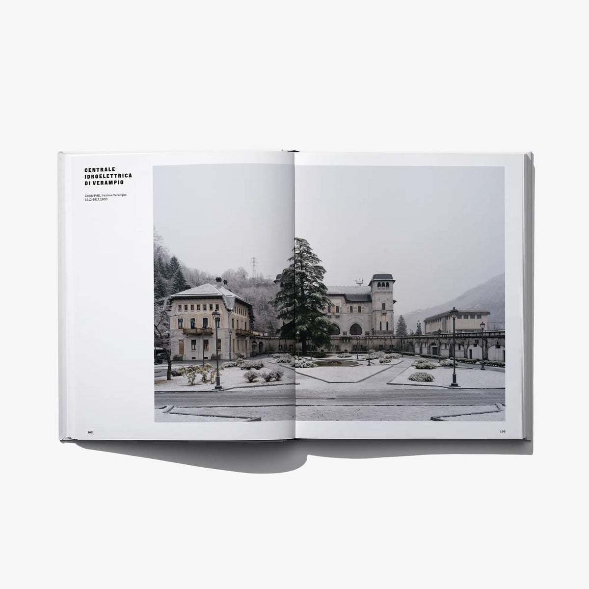 Open hardcover book featuring a monochrome landscape with buildings and hills.