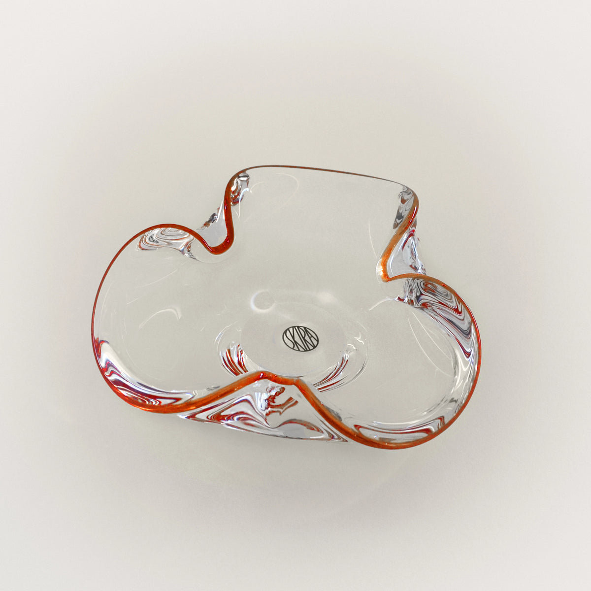 Clear glass tray with red accents, curved leaf shape and small center emblem