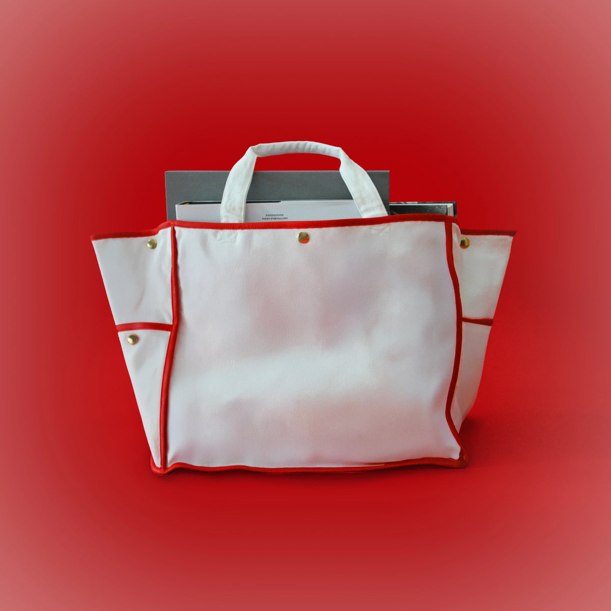 White canvas tote bag with red trim, top handles, and gold hardware