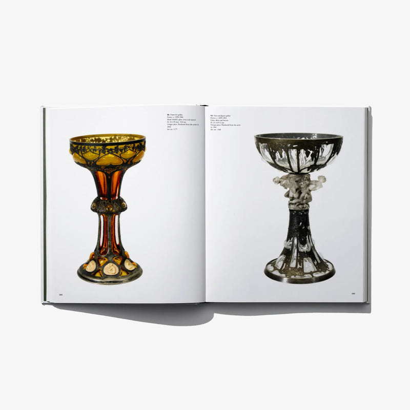 Open art book with two chalice-like objects in amber and dark gray glass
