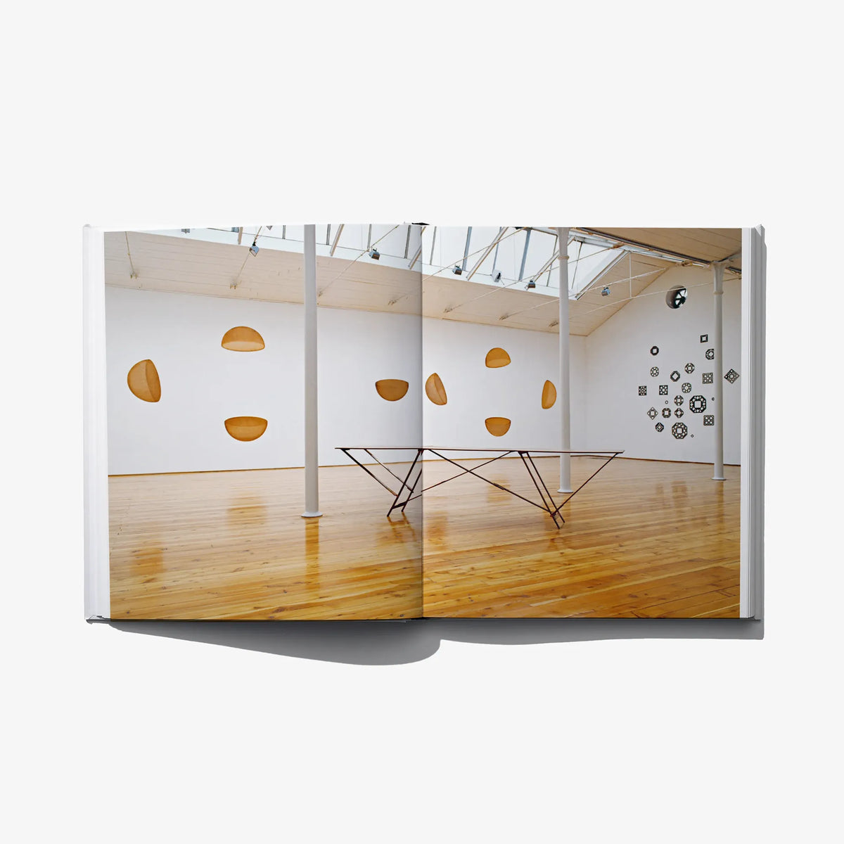 Italian edition art book open spread showing gallery room with hanging gold lamps