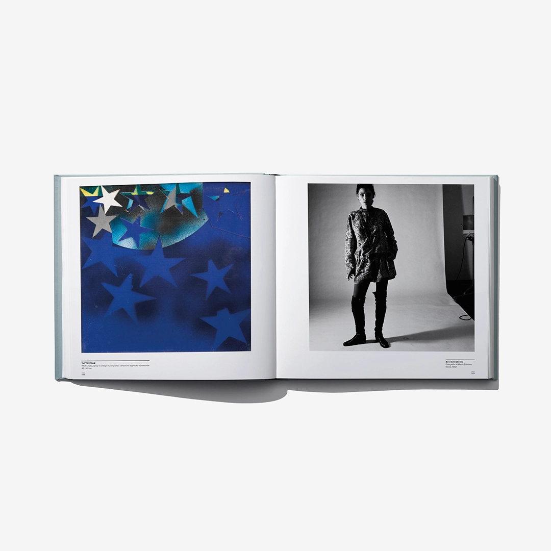 Open art catalog book showing blue star artwork and a standing black-and-white portrait