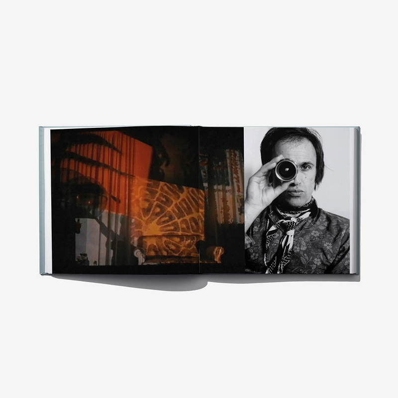 Open art catalog book with orange artwork and black-and-white portrait holding a camera