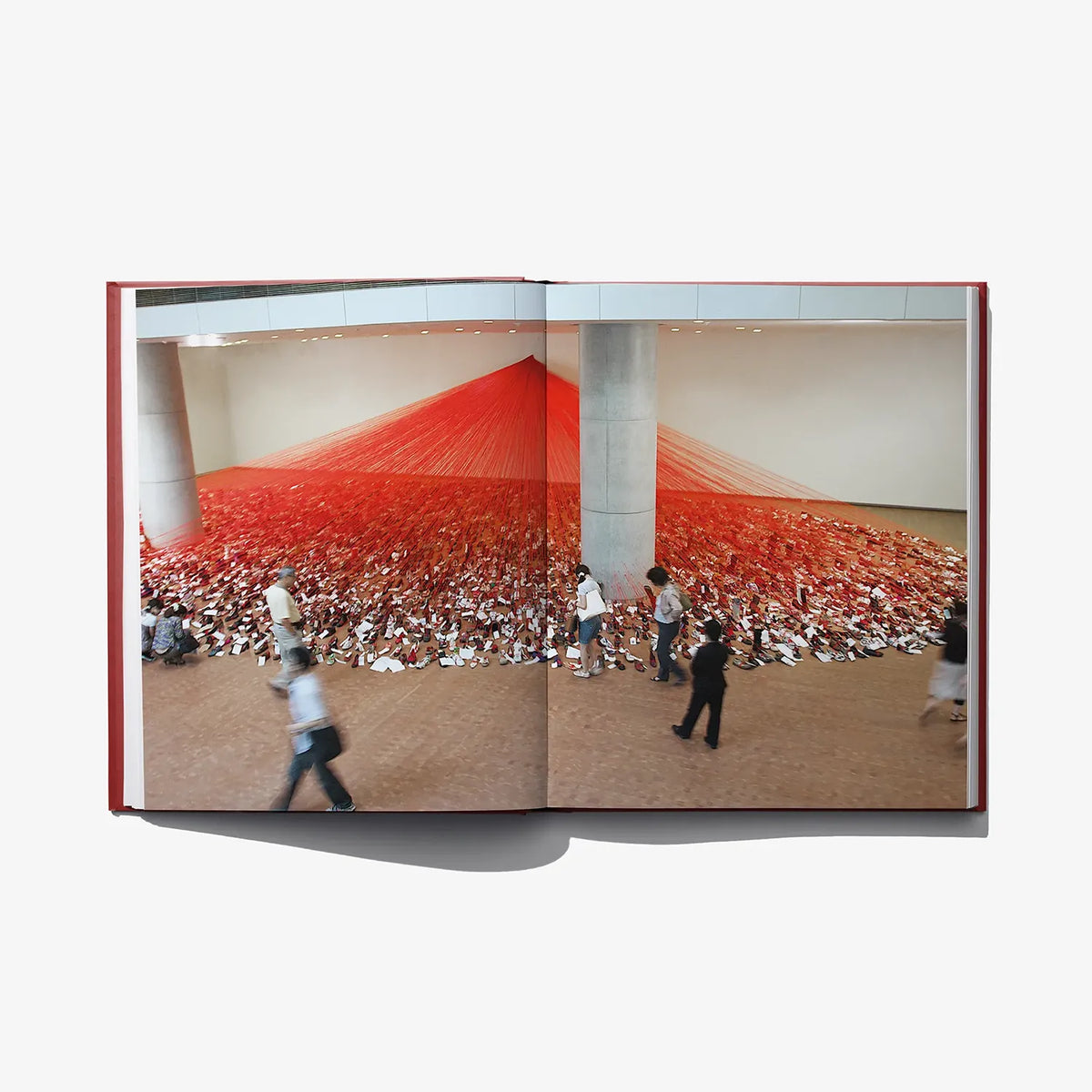 Open art book spread showing red installation room with people walking, plus white margins