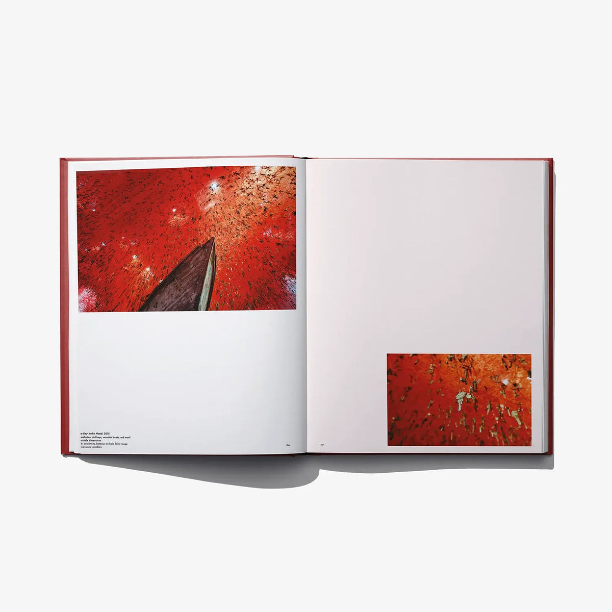 Open art book spread with small red abstract artwork panels on left and right pages