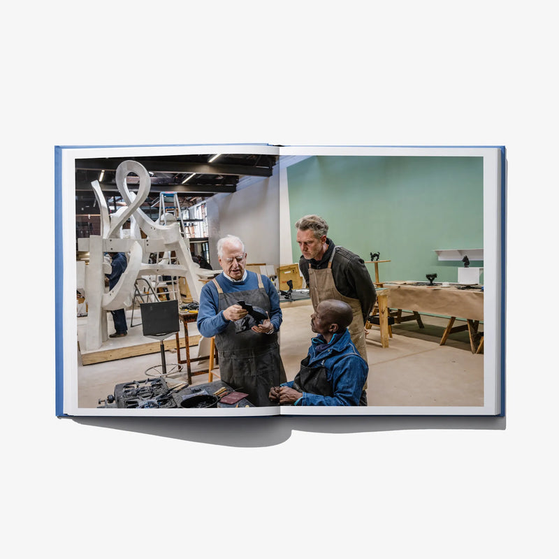 Open art book spread showing a workshop scene with people at work